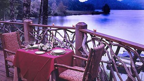 A dining table set with plates, glasses, and a vase of flowers on a deck with a wooden railing overlooking a lake. - Club Lodges at Trillium - 3 Bedroom Presidential (Cashiers)