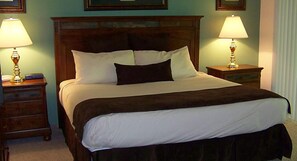 A neatly made bed with a dark headboard, two bedside tables with lamps, and a framed picture above the bed.