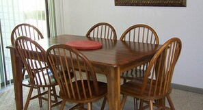 A wooden dining table with six chairs, a red placemat, and a framed picture on the wall.