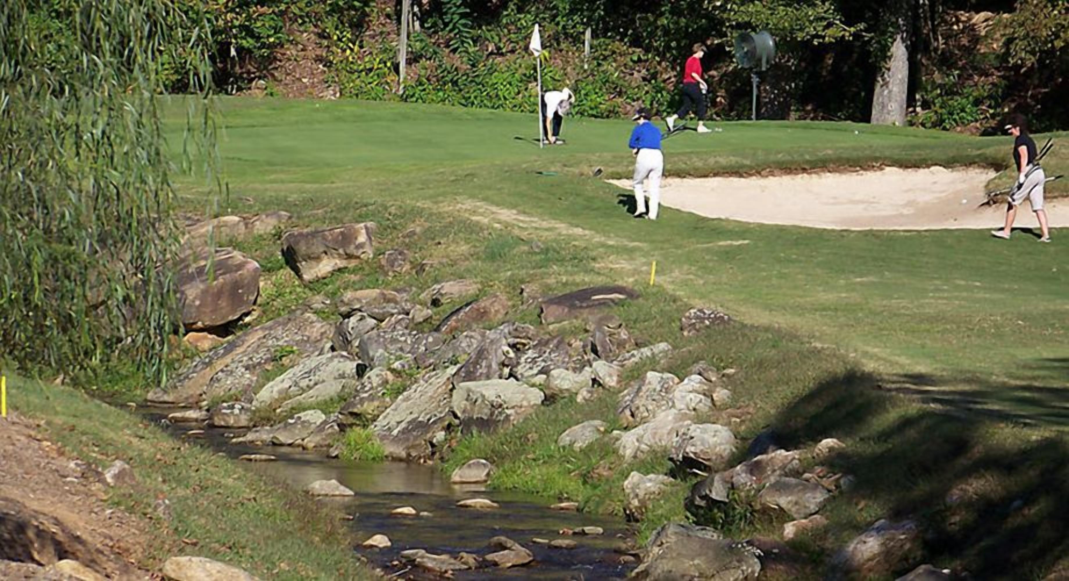 Un parcours de golf avec un ruisseau, des rochers et des bunkers de sable.