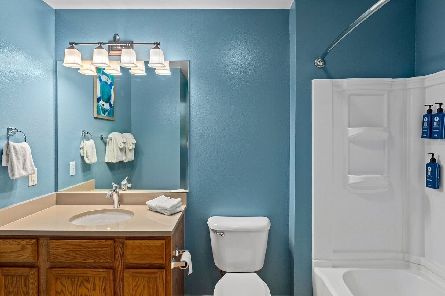 Une salle de bain avec un lavabo, des toilettes et une douche. Des serviettes sont accrochées au mur et des articles de toilette sont posés sur une étagère.