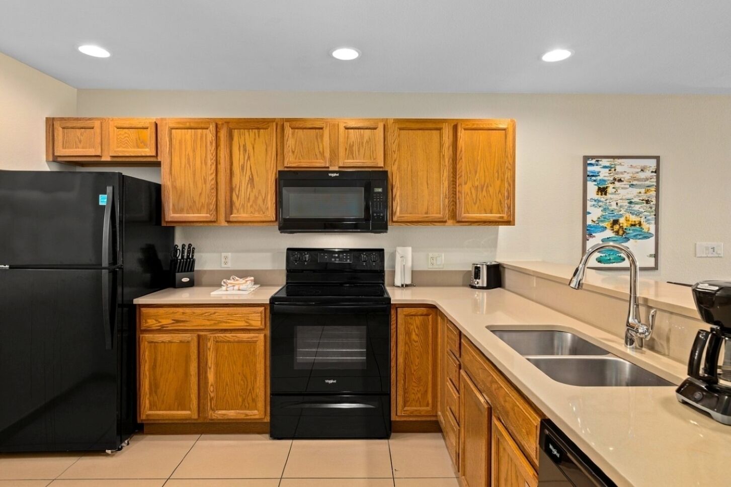 A modern kitchen with wooden cabinets, a black refrigerator, a microwave, an oven, a sink, and a coffee maker.