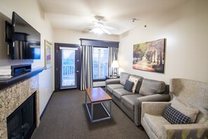 A hotel room with a flat-screen TV, a ceiling fan, a fireplace, a sofa, a coffee table, and a painting.