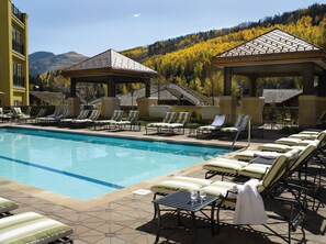 A pool area with lounge chairs and gazebos, surrounded by mountains and autumn foliage.