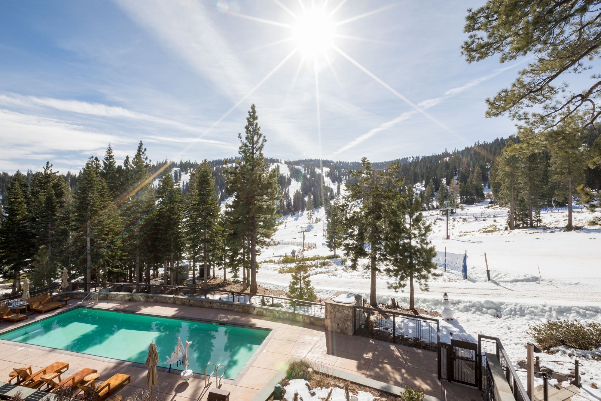 A pool area with lounge chairs and a view of a snowy mountain landscape.