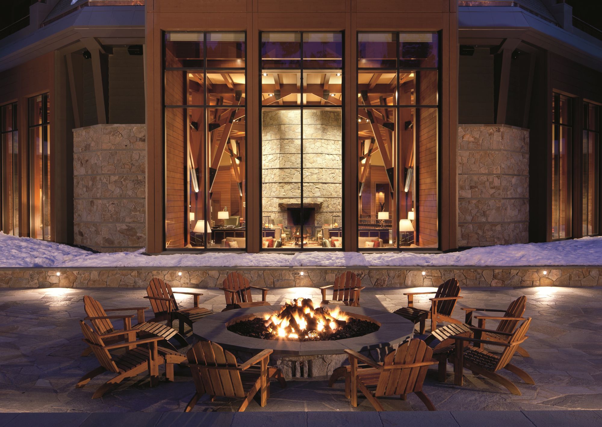 A building with a stone facade, large windows, and a fire pit with chairs in front.