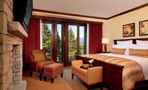 A hotel room with a large bed, a fireplace, a sofa, and a balcony with a view of trees and mountains. - Lake Tahoe | Luxury Ski Retreat | Ski + Spa | 4BR Sleeps 10 (Truckee)