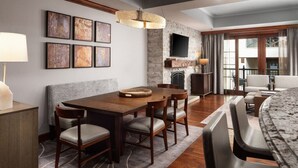 A modern dining area with a wooden table and chairs, a fireplace, and a flat-screen TV mounted on a stone wall. - Ritz Carlton Club, San Fransico - 1 Bedroom (San Francisco)