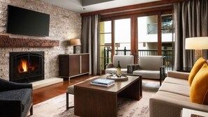 A living room with a fireplace, a flat-screen TV mounted on a brick wall, a sofa, a coffee table with a book, and a view of a balcony with outdoor furniture. - Ritz Carlton Club, San Fransico - 1 Bedroom (San Francisco)