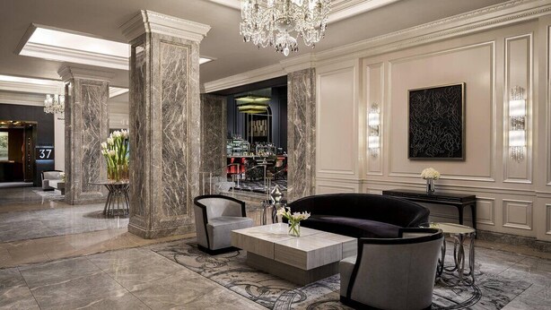 Un hall d’entrée spacieux, orné de colonnes en marbre, d’un lustre et d’un espace salon moderne.