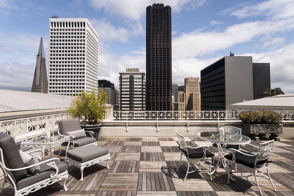 A rooftop terrace with outdoor furniture, a view of the city skyline, and a white railing.