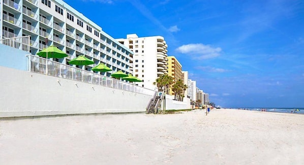 A beachfront hotel with multiple balconies, a sandy beach, and a clear blue sky.