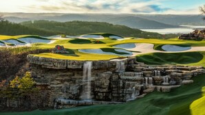 Un parcours de golf agrémenté d’une cascade et offrant une vue sur des collines lointaines.