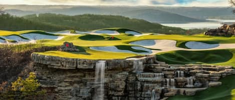 Un parcours de golf agrémenté d’une cascade et offrant une vue sur des collines lointaines.
