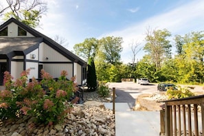 A modern house with a stone pathway leading to the entrance, surrounded by lush greenery and a clear sky.