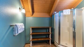 A bathroom with a wooden shelf, a towel rack, and a glass shower enclosure.