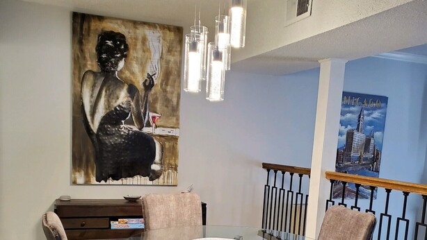 A dining area with a glass table, four upholstered chairs, a painting on the wall, and a Chicago-themed poster. - Relaxing condo getaway (Huntsville)