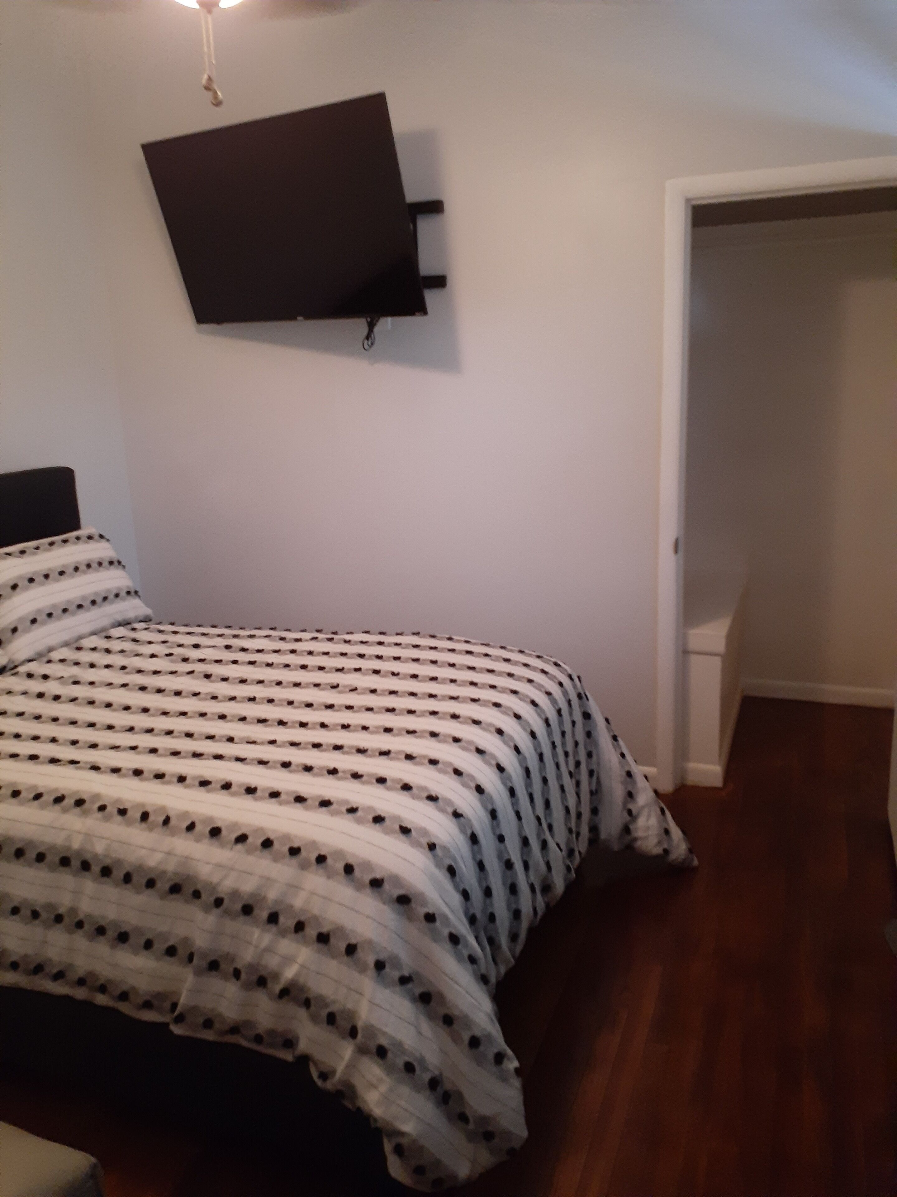 A bedroom with a bed, a flat-screen TV mounted on the wall, and a door leading to another room.