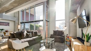 A modern living room with large windows, a flat-screen TV, and a variety of seating options including a sofa and chairs. - Spacious Chic 1Br East Nashville Loft! (Nashville)