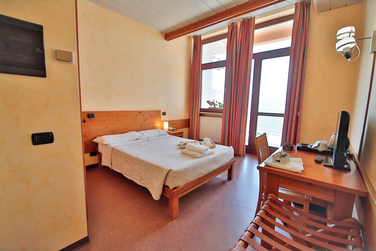 A hotel room with a wooden bed, a desk with a computer, and a chair.
