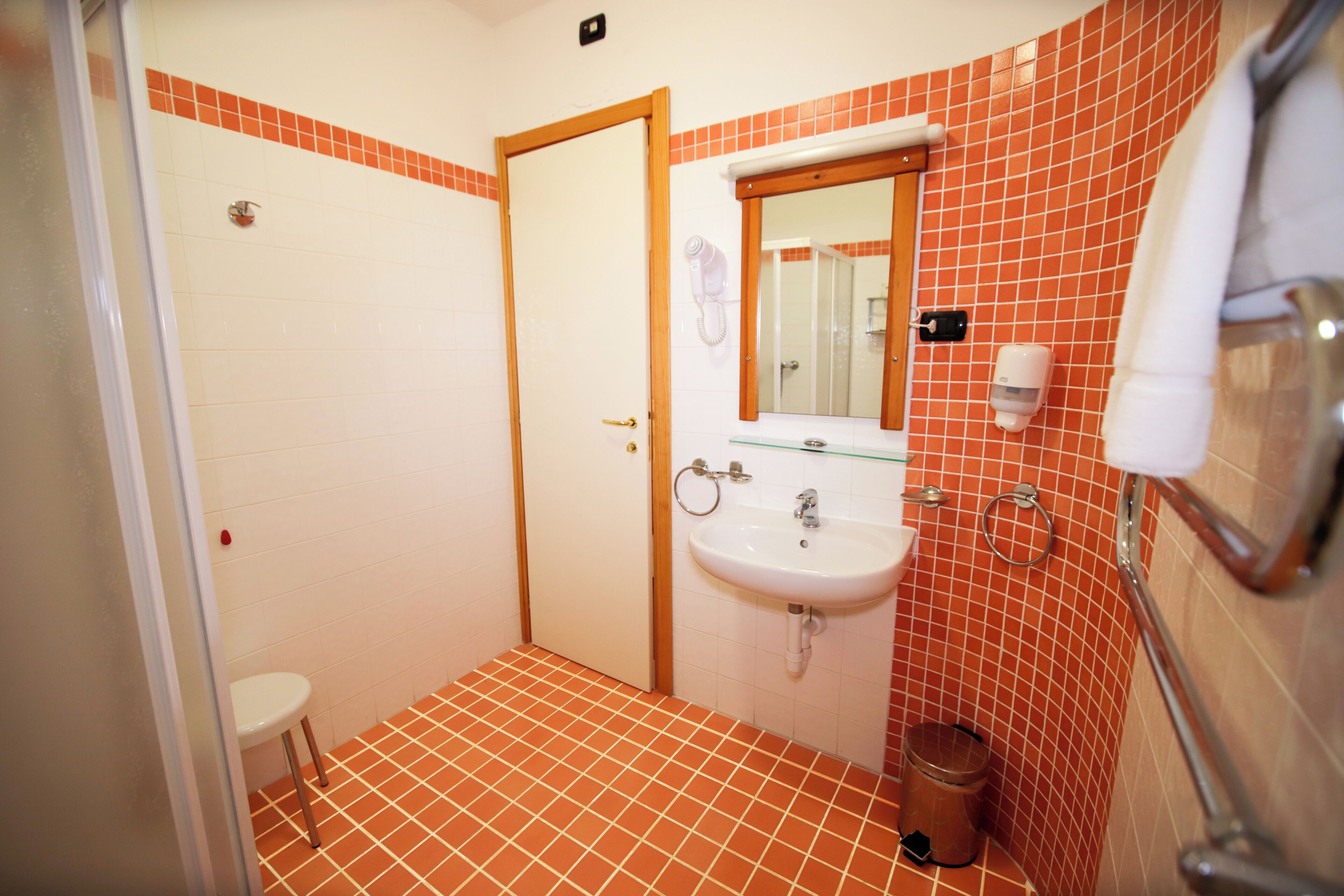 Un baño con lavamanos blanco, espejo, toallero y un pequeño cubo de basura.