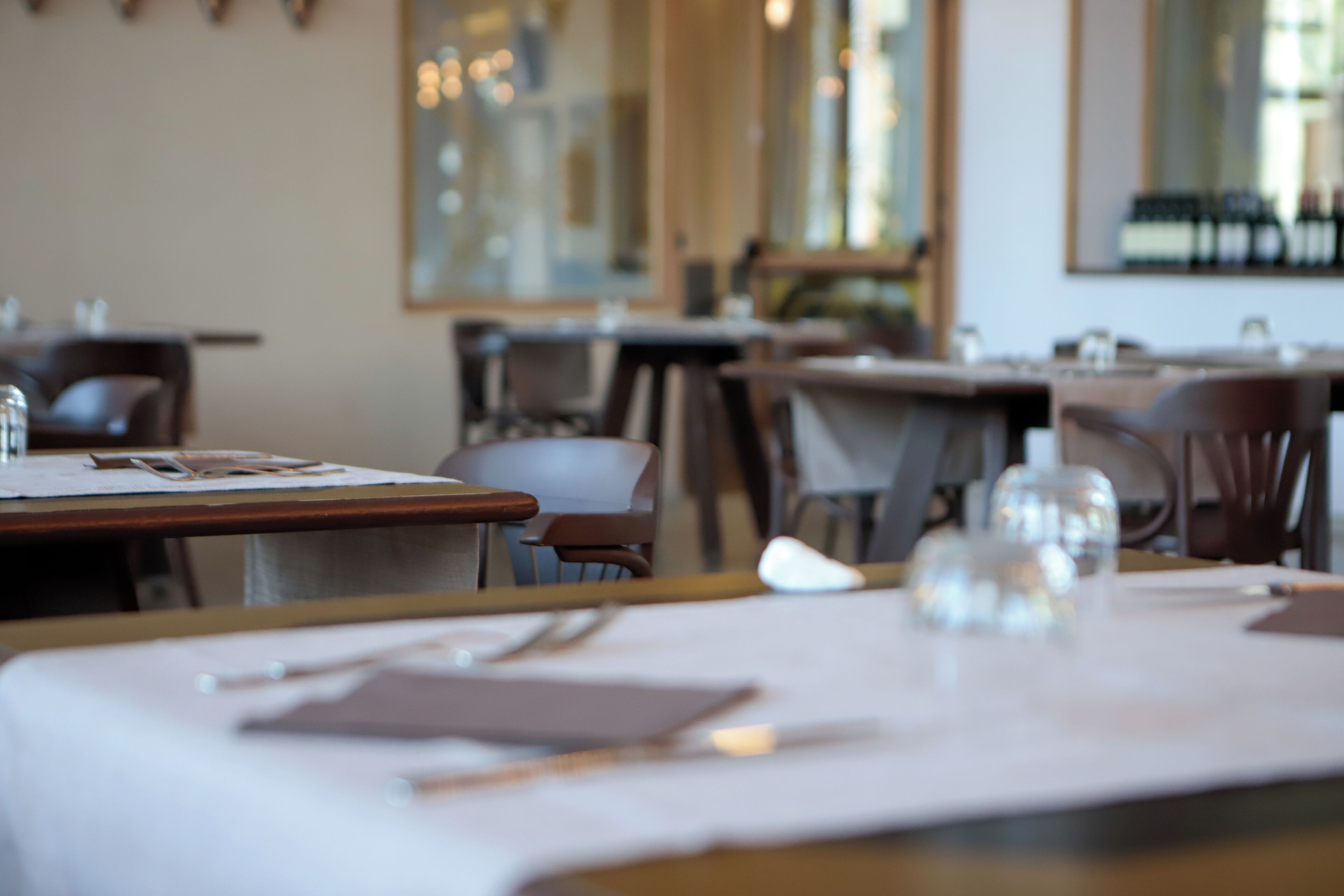 Un interior de restaurante con mesas dispuestas para comer, sillas y un amplio ventanal al fondo.