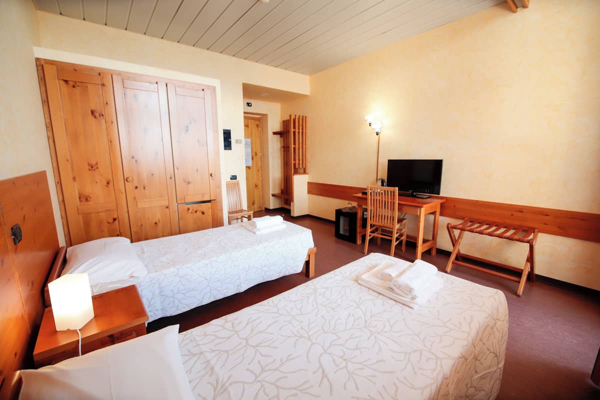 A hotel room with two beds, a desk, a chair, a television, and wooden furniture.
