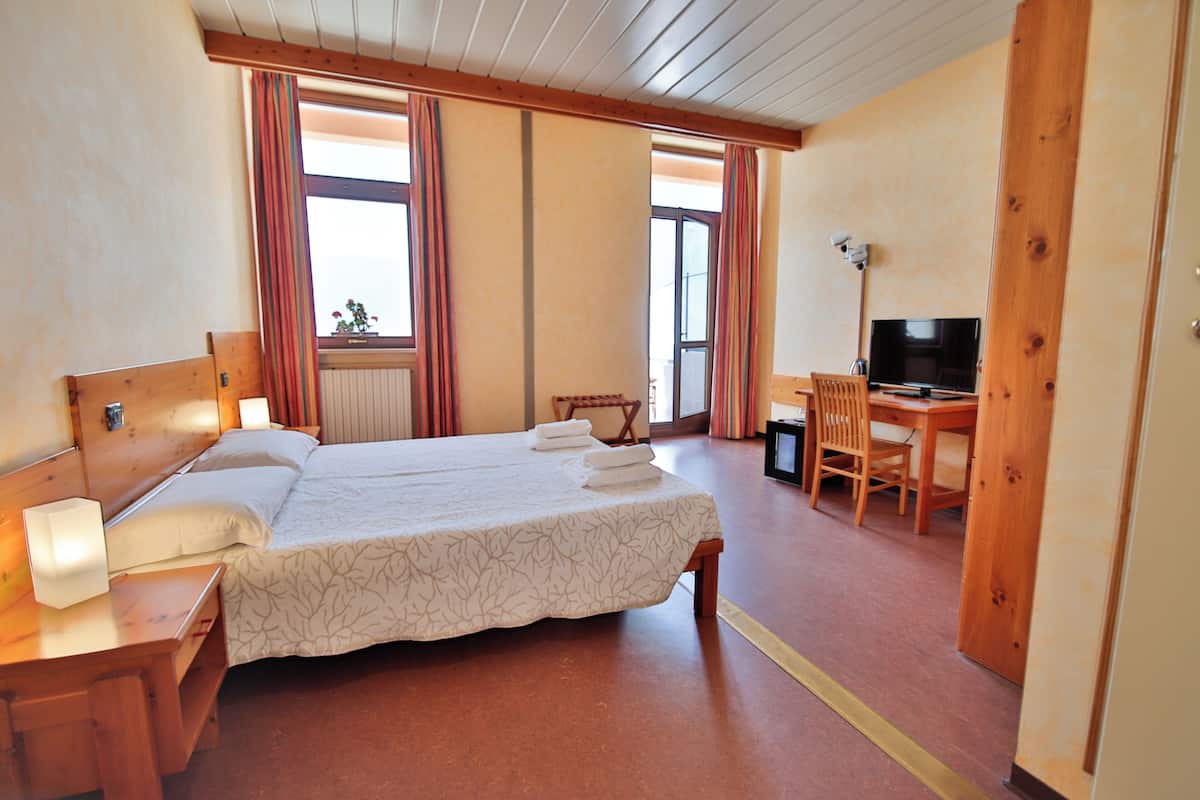 A hotel room with a double bed, a desk with a chair, a television, and a window with curtains.