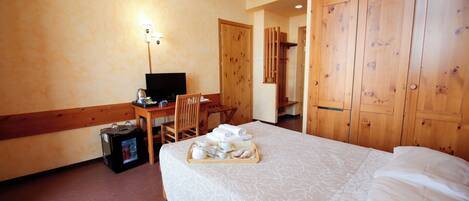 A hotel room with a bed, a desk with a computer, a chair, a tray with breakfast items, and wooden wardrobes.