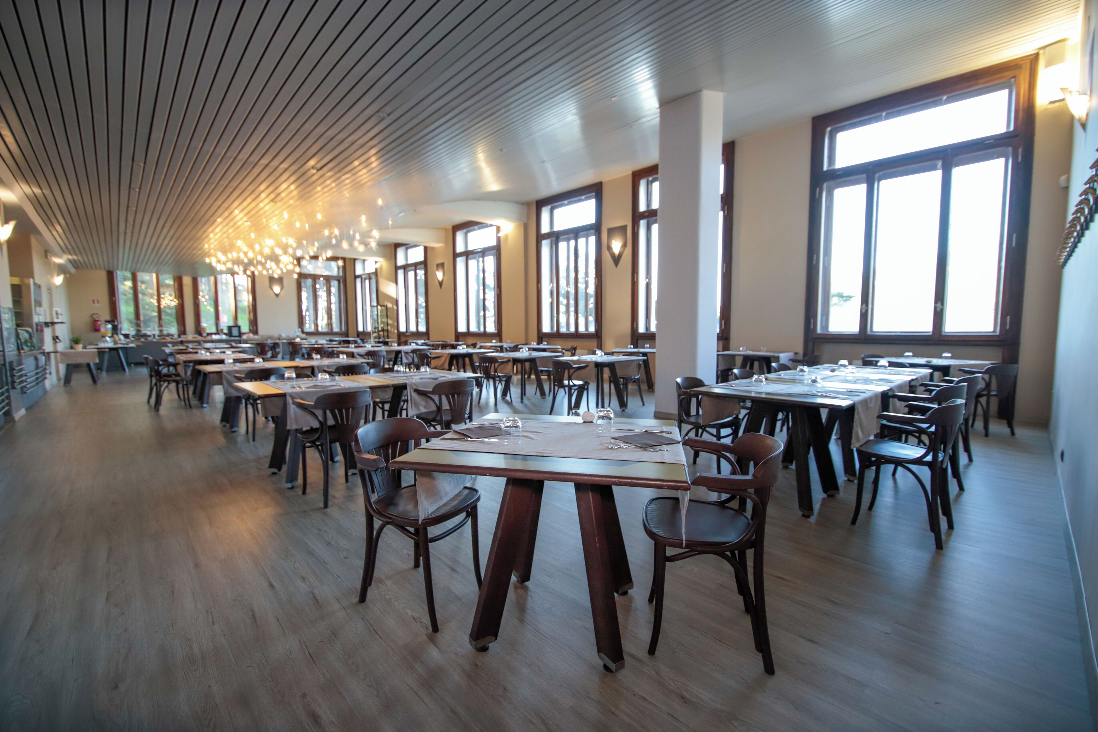 Un restaurant spacieux, doté de nombreuses tables et chaises, de grandes fenêtres et d’un plafond en bois.