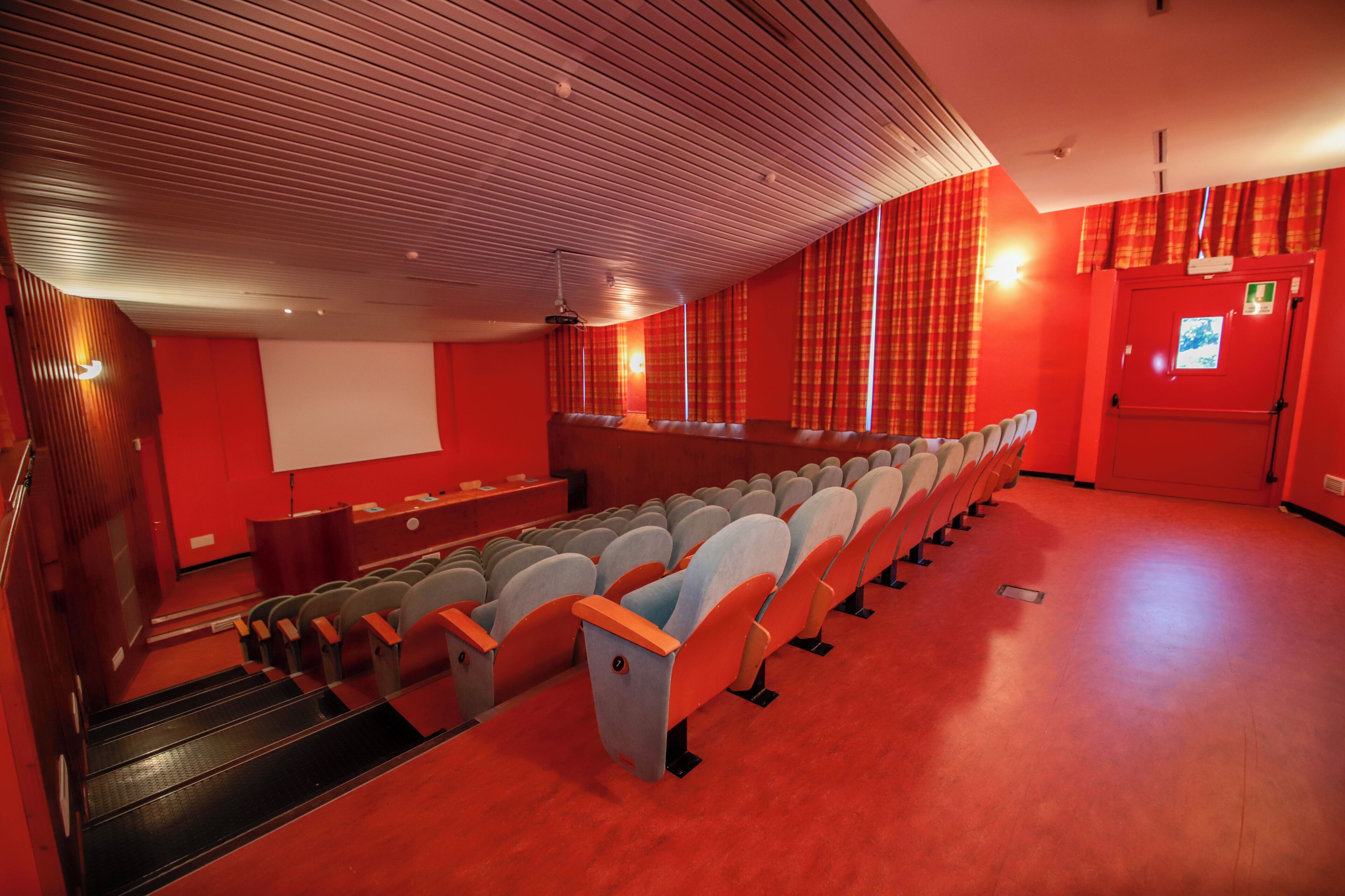 Ein Kino mit Sitzreihen, einer Leinwand und einer roten Wand.