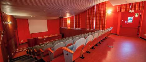 Ein Kino mit Sitzreihen, einer Leinwand und einer roten Wand.