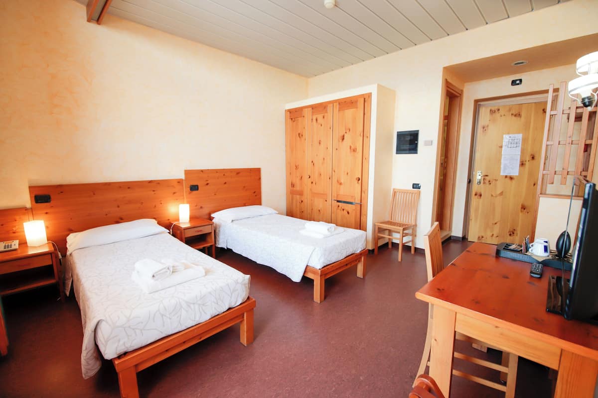 A hotel room with two wooden beds, a wooden desk, and a chair.