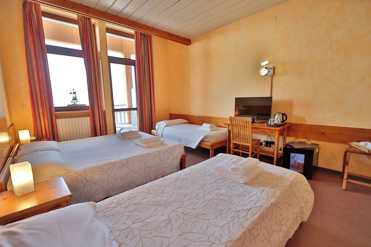 A hotel room with two beds, a desk, a chair, a television, and a small table with a lamp.