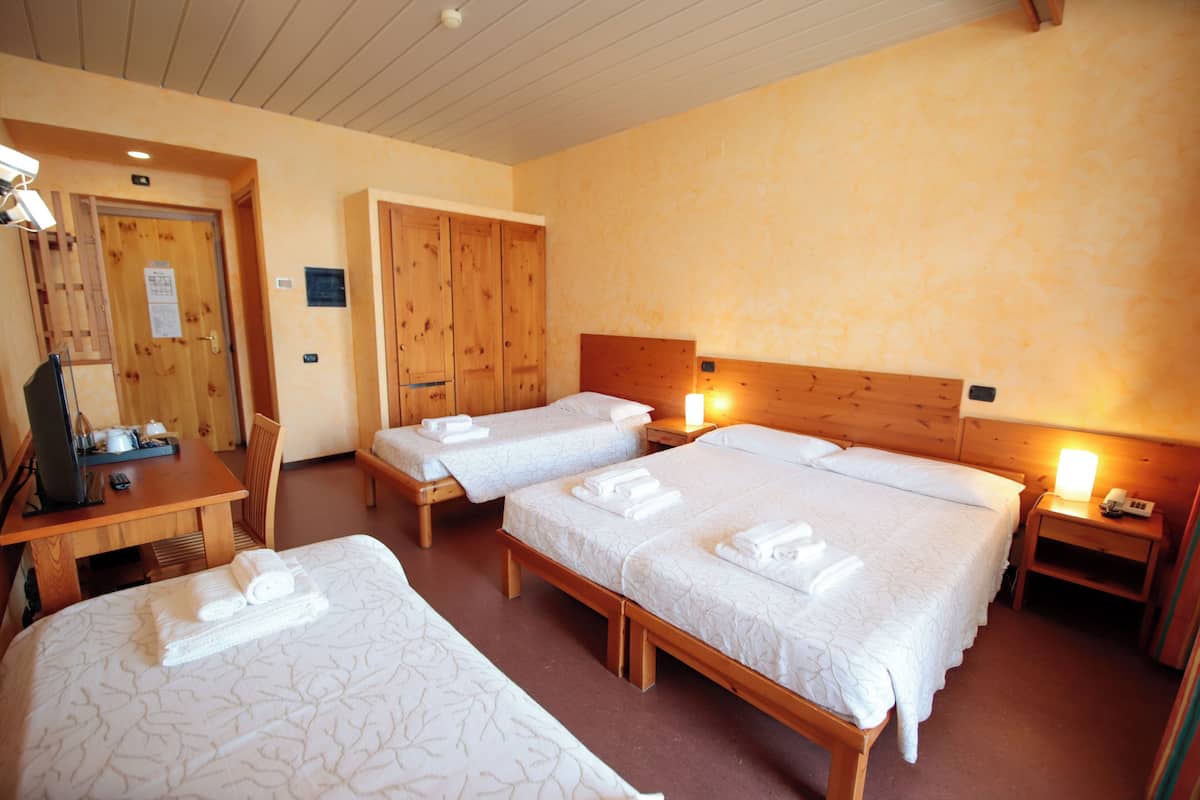 A hotel room with three single beds, wooden furniture, and a desk with a computer.