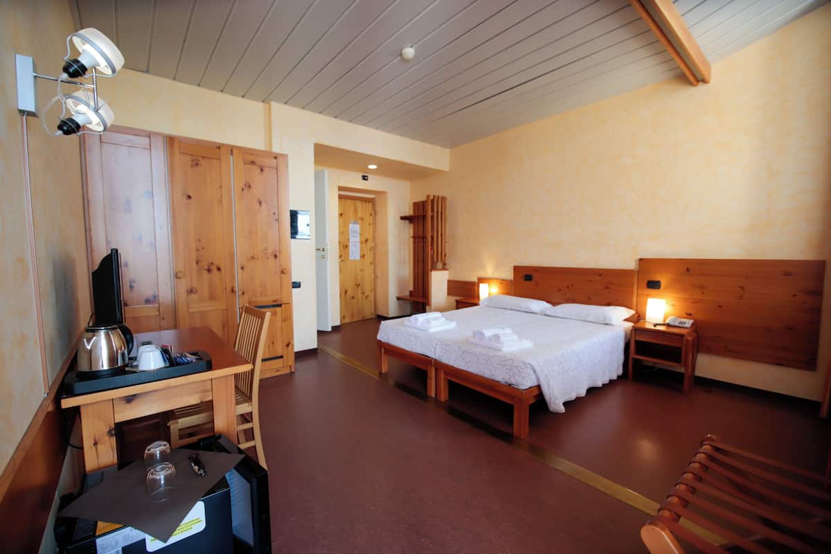 A hotel room with a wooden desk, a bed with white linens, a nightstand with a lamp, and a wooden chair.