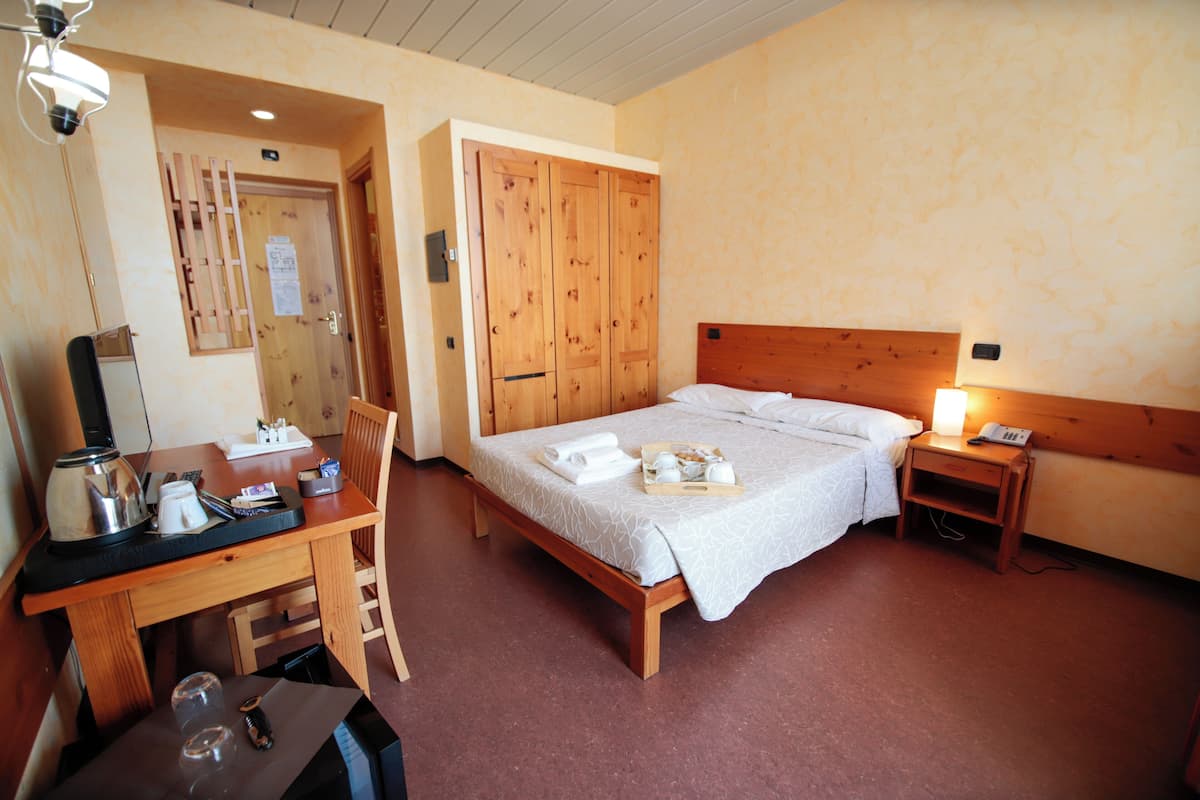 A hotel room with a wooden bed, a desk with a coffee maker, and a nightstand with a lamp.