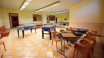 Una stanza con due tavoli da calcio balilla, un tavolo da ping pong e un tavolo da scacchi. Ci sono diverse sedie e un tavolo con dei libri.
