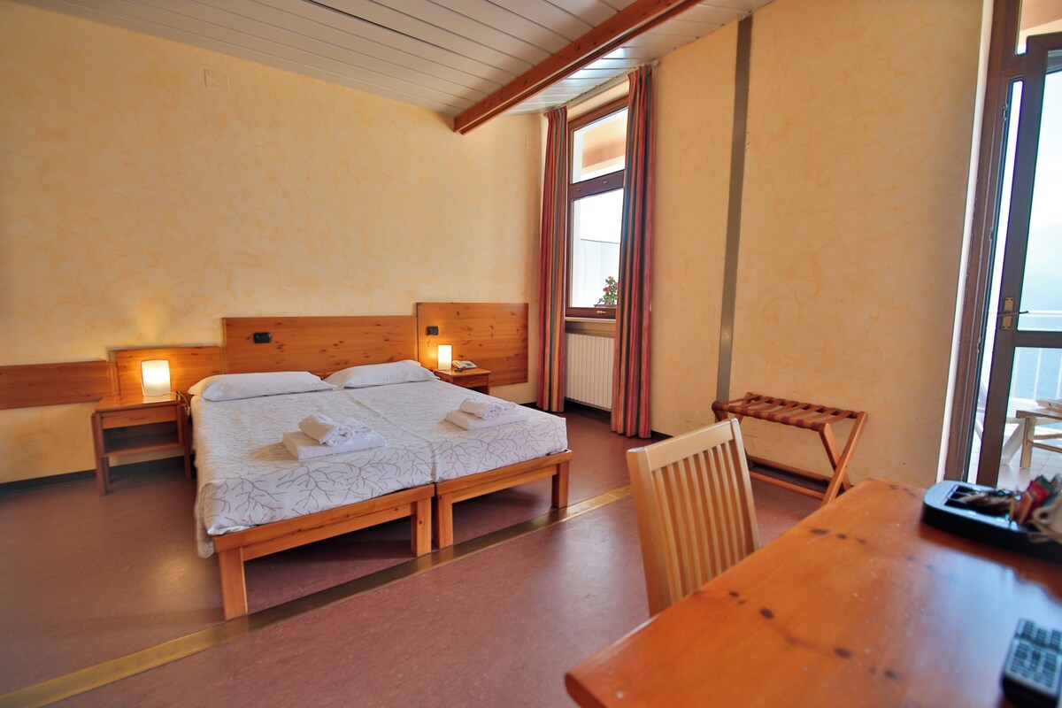 A hotel room with a wooden bed, bedside tables, a wooden chair, and a table with a remote control.