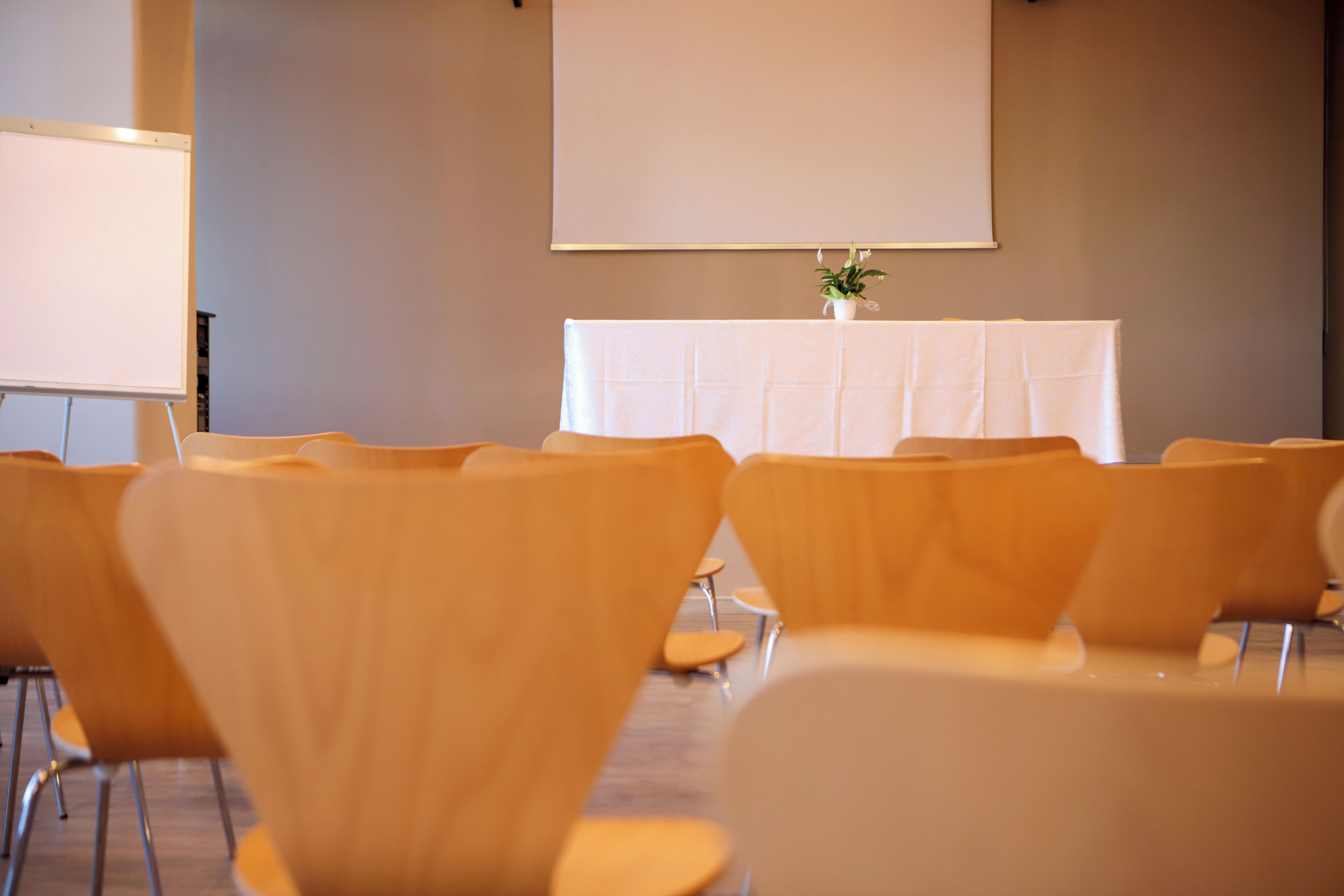 Une salle de conférence avec des rangées de chaises, un tableau blanc et une table ornée d’une plante.