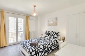 A bedroom with a bed, bedside tables, a desk, a hanging light fixture, a window with curtains, and a wall-mounted picture. - ⭐️MAGNIFIQUE T5 GARE ST CHARLES/VIEUX PORT/2 BALCONS⭐️CLIMATISÉ (Marseille)