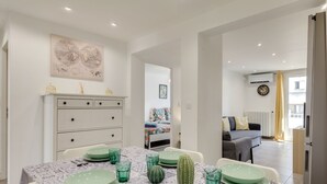 A dining area with a table set for four, a white dresser, and a bed in the background.