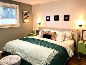 Una camera da letto ordinata con un letto, due comodini, un tavolino e luci fissate al muro.