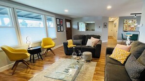 Un salon moderne avec une table basse en verre, un canapé et un fauteuil jaune.