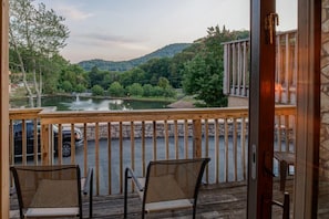 Enjoy a serene lakeside view from this deck, featuring two comfortable chairs and a scenic backdrop.
