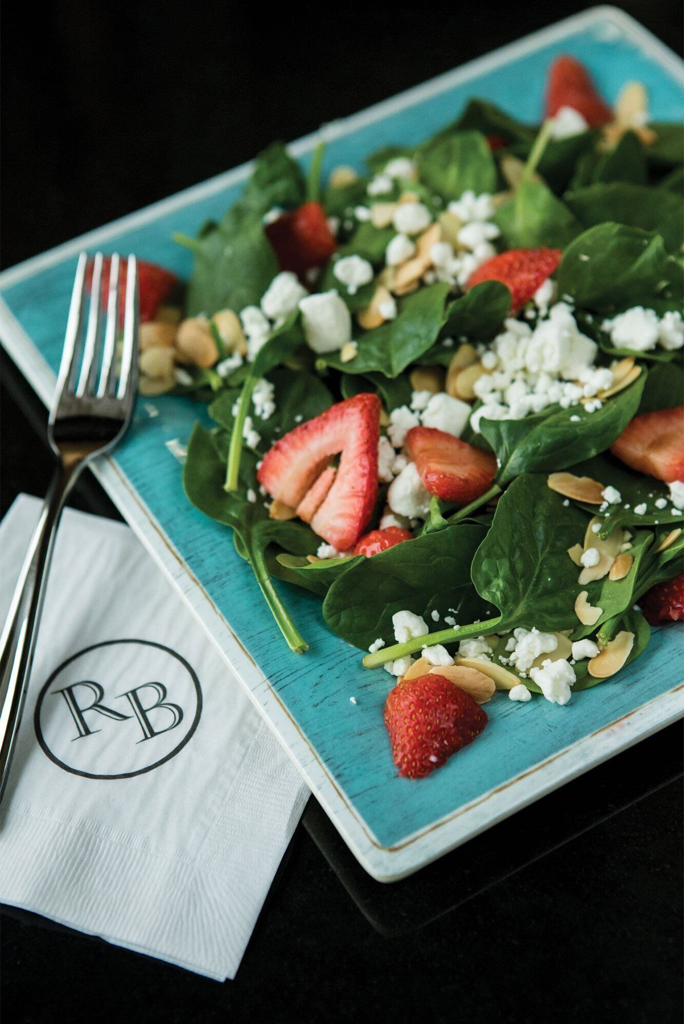 A plate of spinach salad with strawberries and feta cheese.