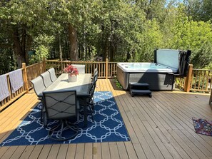 A deck with a dining table, chairs, and a hot tub.