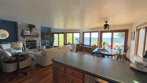 A spacious living area with a fireplace, a dining table with chairs, and large windows offering a view of the ocean. - 5BR Waterfront Retreat – Experience Door County’s Best Season, Fall! (Sturgeon Bay)
