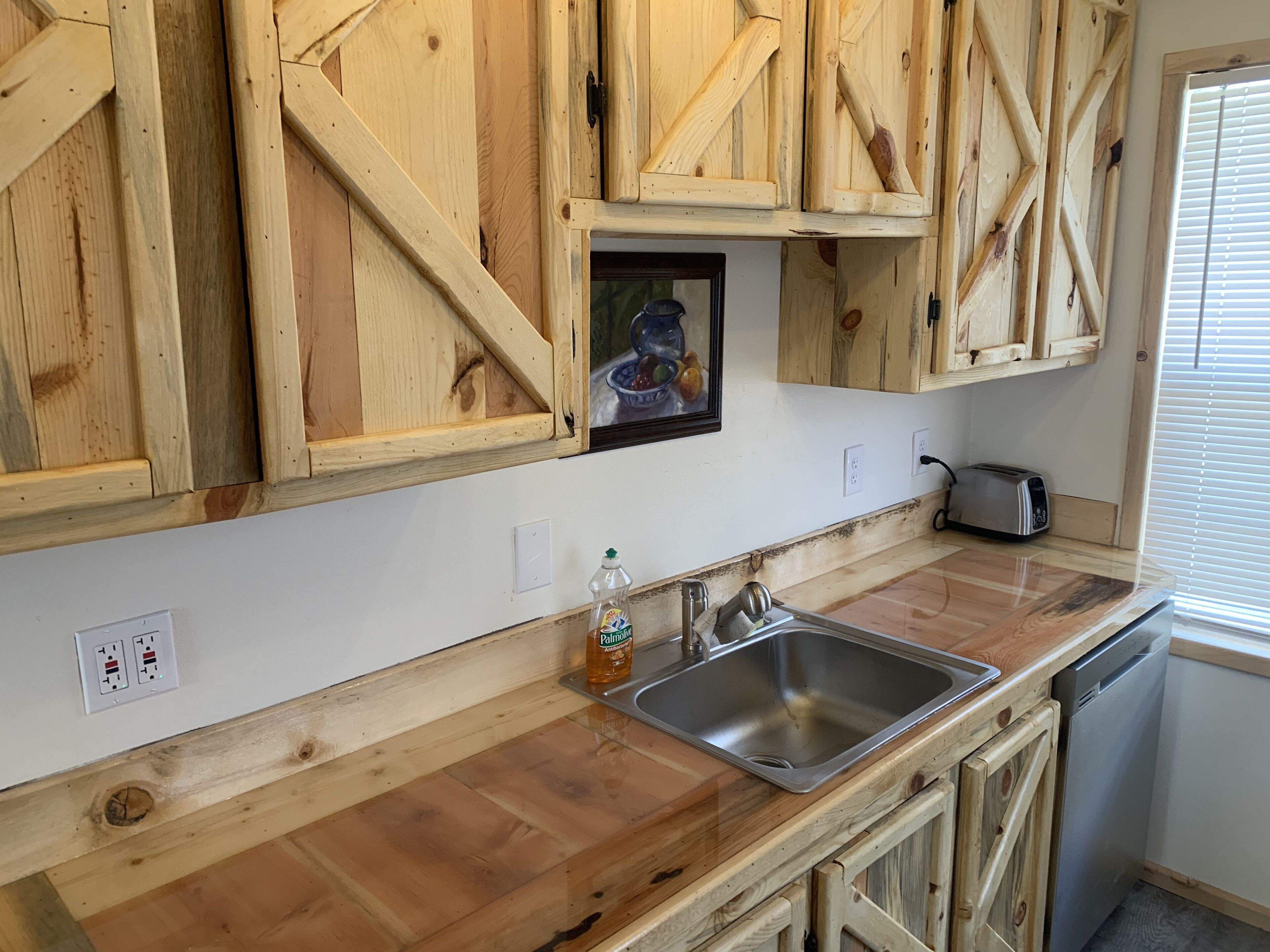 Une cuisine avec des meubles de rangement en bois, un évier en acier inoxydable, un grille-pain et un lave-vaisselle.