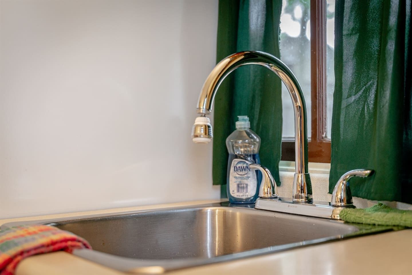 A stainless steel kitchen sink with a single faucet, a dish soap bottle, and a green towel.